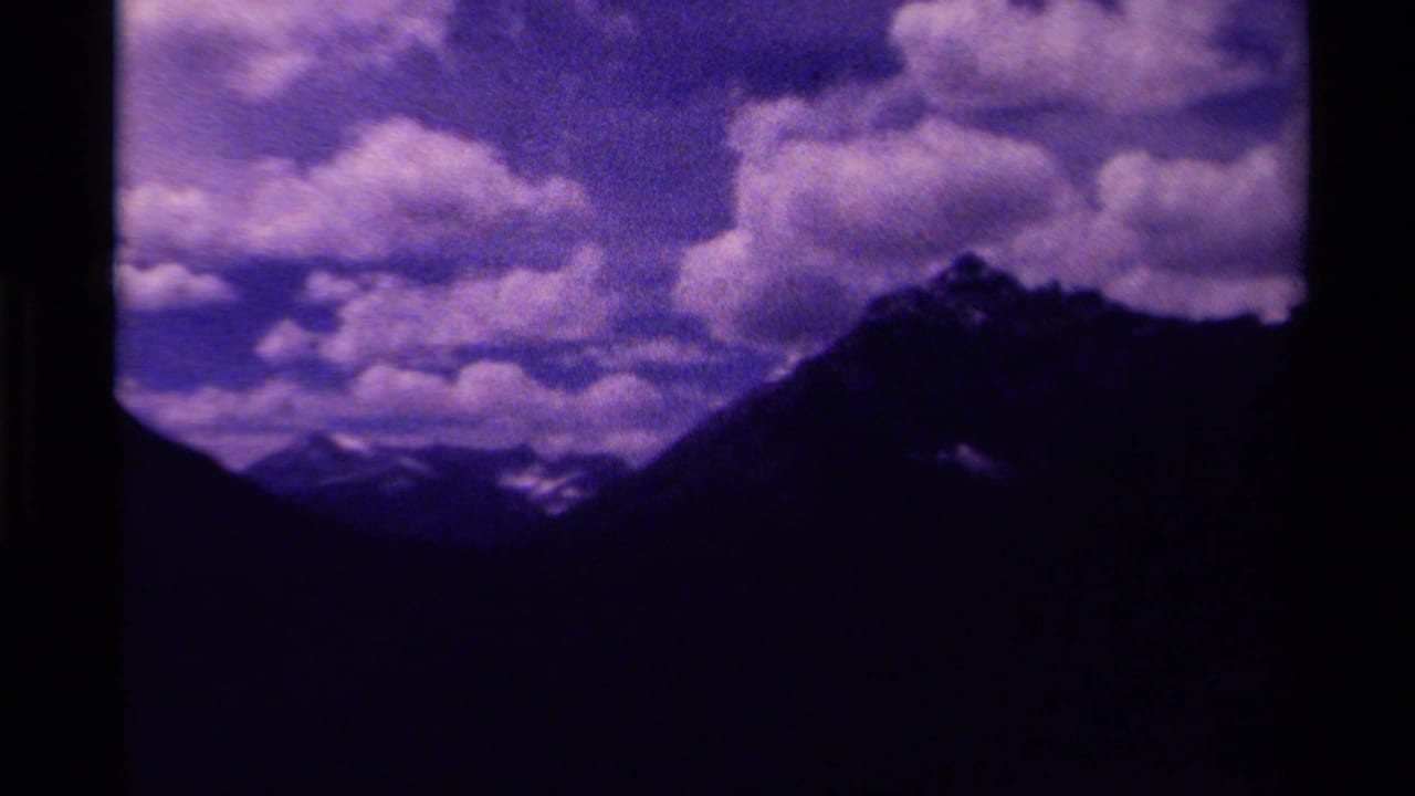 Dark mountain ridge beneath large clouds in a purple-blue sky.
