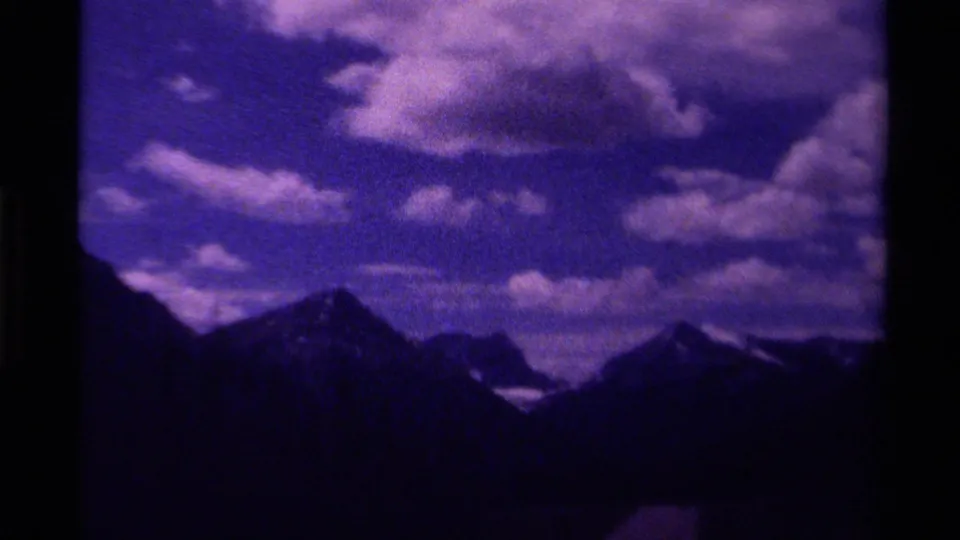 1979 Canadian 8mm frame showing multiple mountain peaks beneath large clouds, with dark foreground terrain and a purple-blue cast.