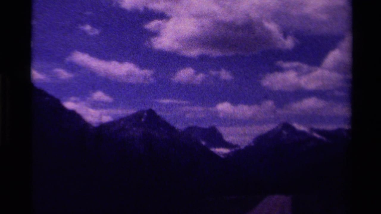 Dark mountain peaks under a cloudy purple-blue sky on 8mm film.