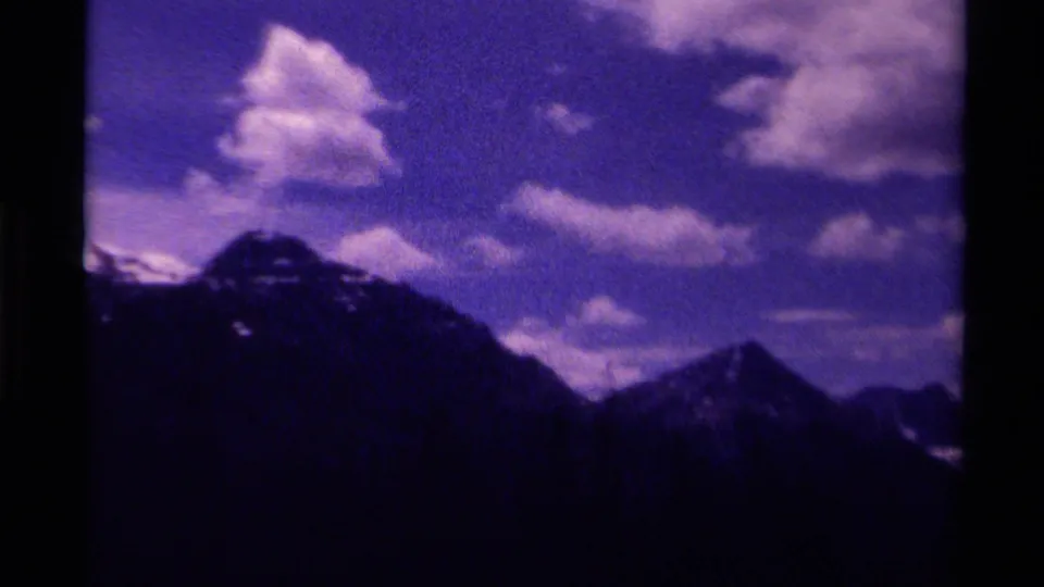 1979 Canada 8mm home-movie frame showing a dark mountain slope with snow flecks below large clouds in a tinted sky.