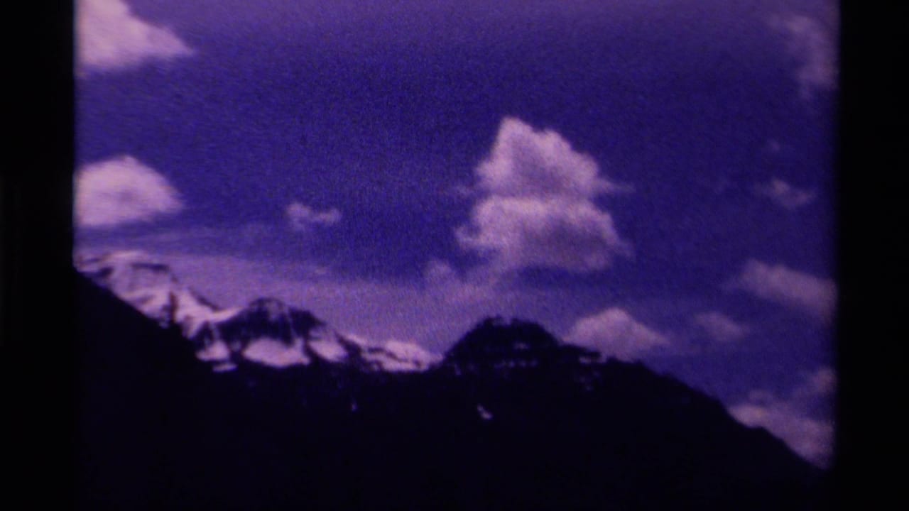 1979 Canada 8mm frame showing a dark mountain silhouette with snowy peaks below a purple-blue sky and scattered clouds.