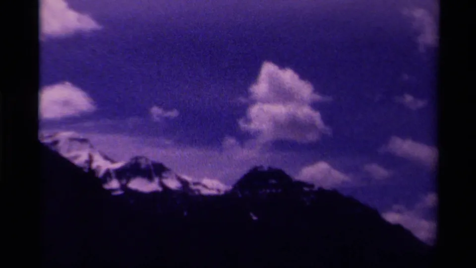 1979 Canada 8mm frame showing a dark mountain silhouette with snowy peaks below a purple-blue sky and scattered clouds.