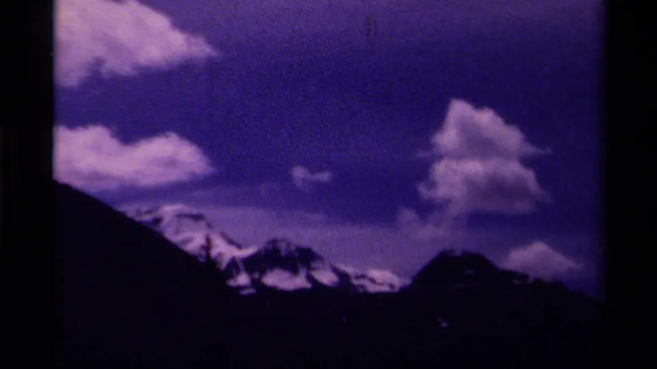 1979 Canada 8mm view of snow-lined mountains beneath large clouds, with visible gate edges and purple color cast.