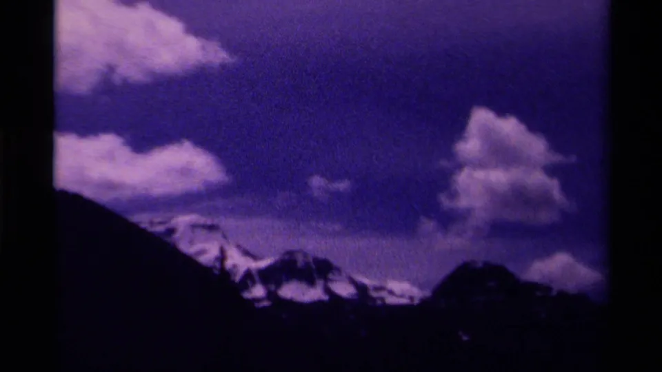1979 Canada 8mm frame showing a dark slope in front of distant snow peaks and bright clouds during the mountain pan.