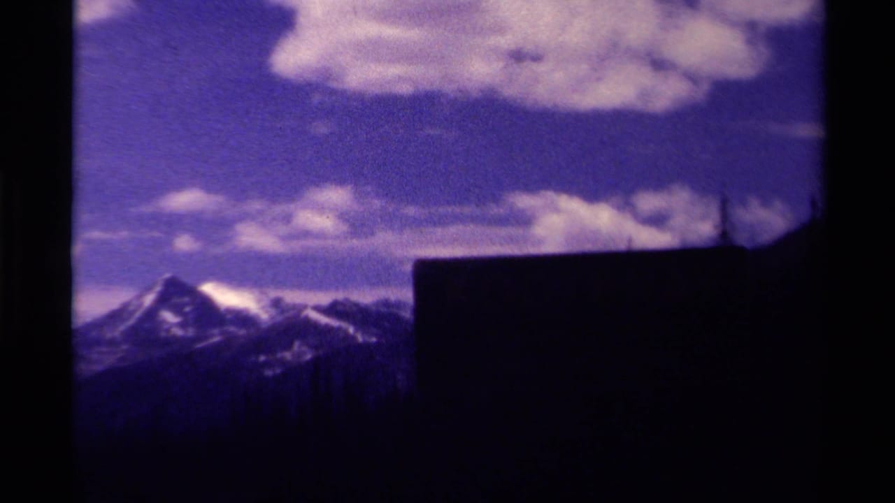 Snow-capped mountain peaks under clouds, partly blocked by a dark foreground structure.