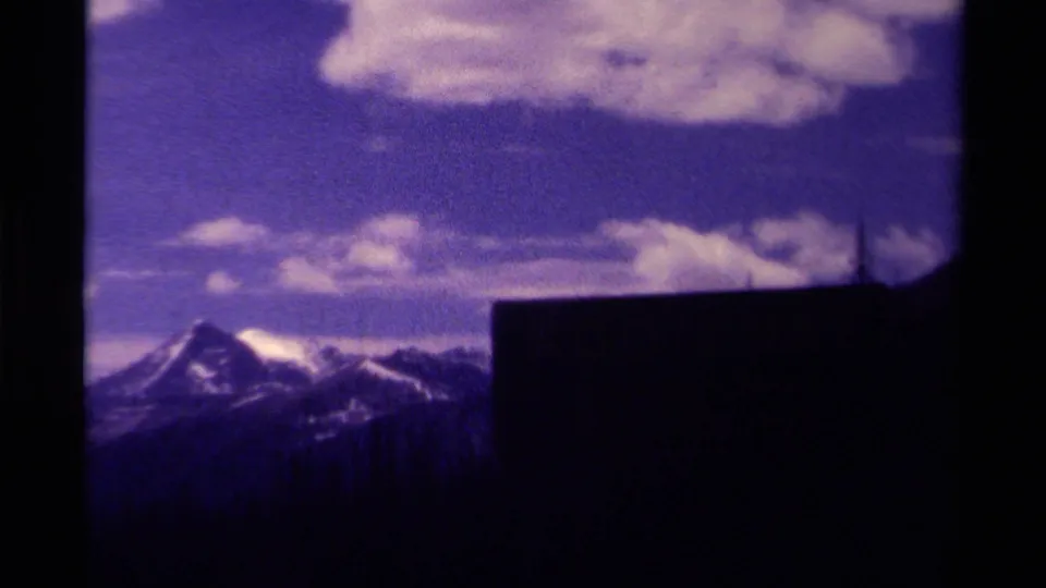 Canadian 8mm travel view of snow-dusted mountains and clouds, partially framed by a large dark foreground shape.