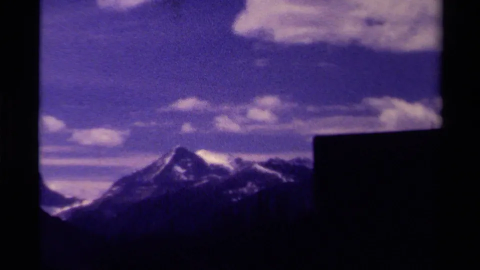 1979 Canada mountain vista on 8mm film, showing a central snow-capped peak, clouds, and a dark foreground structure at the right edge.