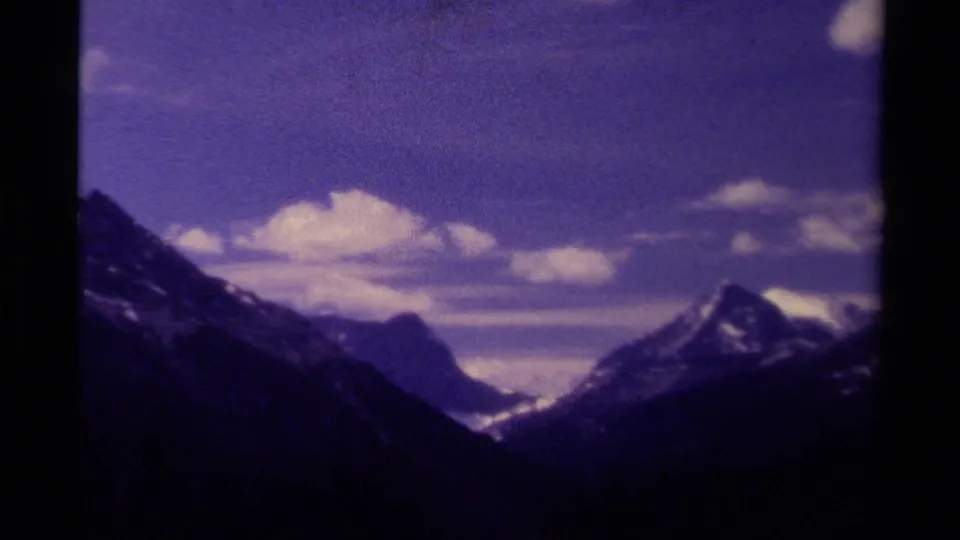 1979 Canadian 8mm view of dark mountain ridges, snow-streaked peaks, and scattered clouds in a purple-tinted sky.