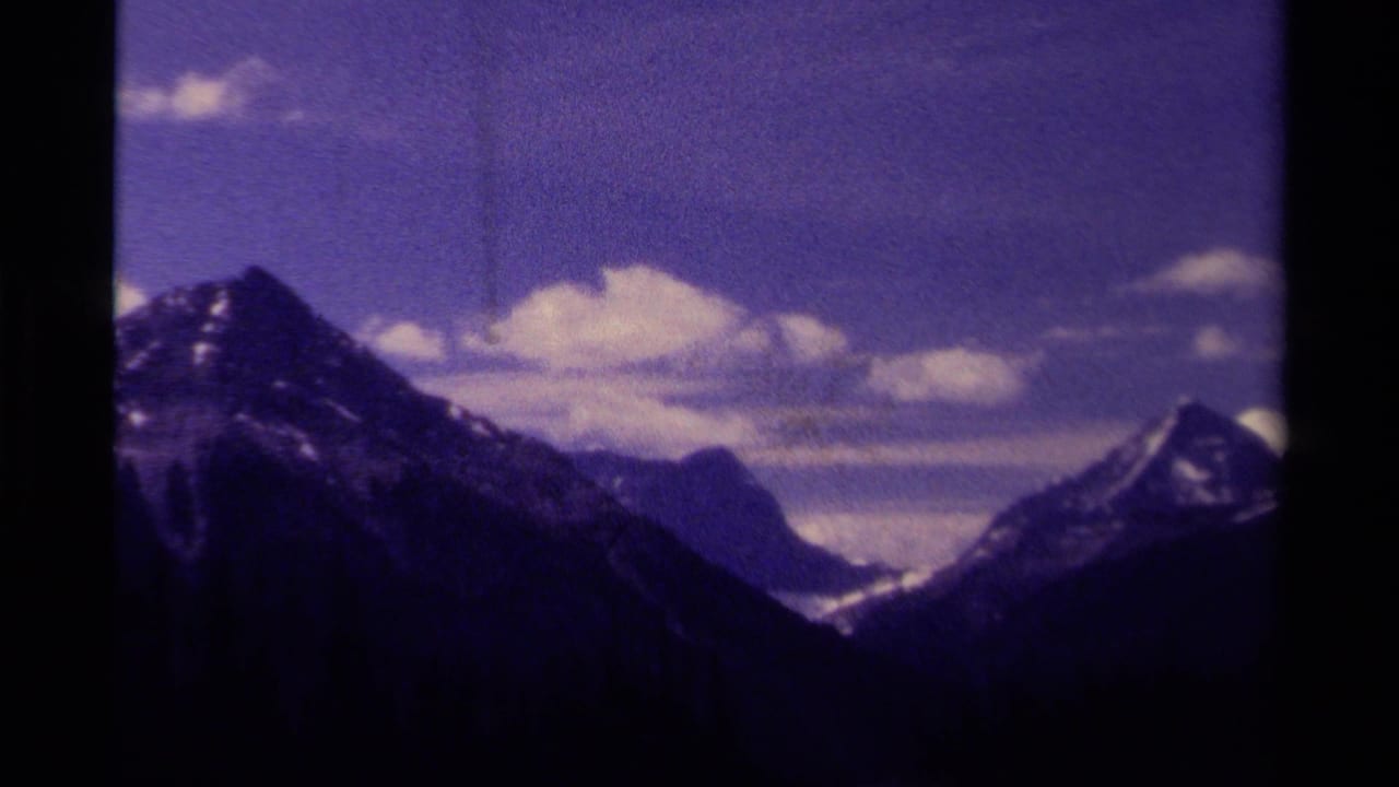 Handheld 8mm frame of a Canadian mountain valley with snow on peaks, dark slopes, and a cloud band across the sky.