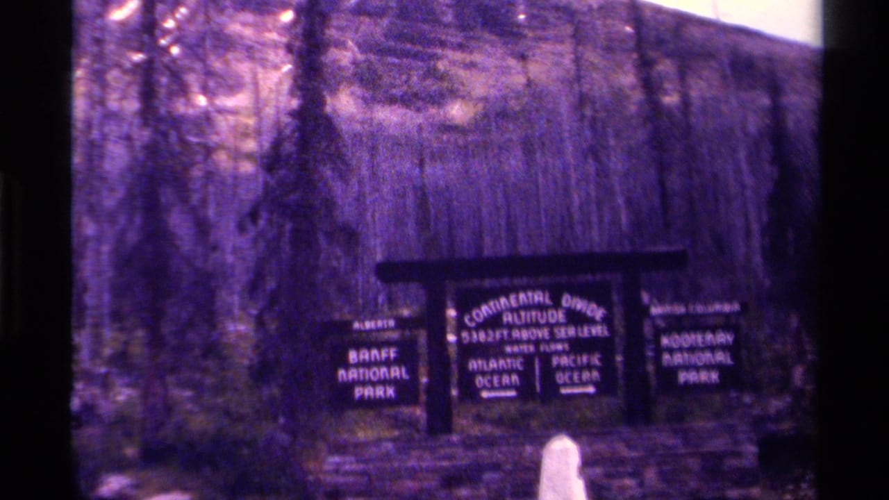 1979 Canada 8mm frame of the Continental Divide sign, with Banff National Park and Kootenay National Park panels readable.