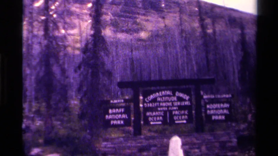 1979 Canada 8mm frame of the Continental Divide sign, with Banff National Park and Kootenay National Park panels readable.