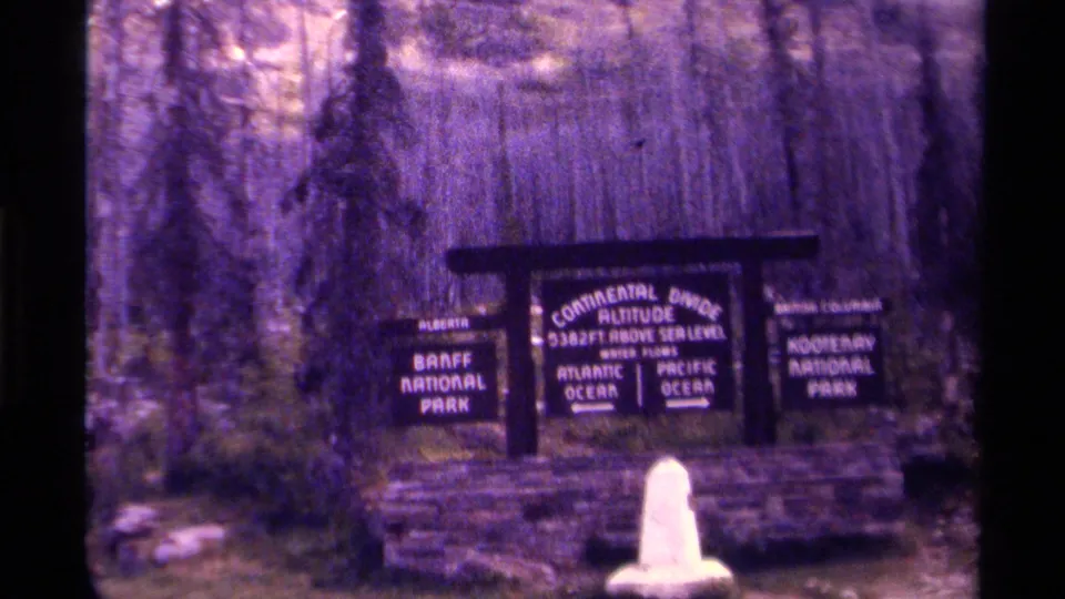 1979 Canada 8mm frame showing the lower part of the Continental Divide sign in a wooded mountain park area.