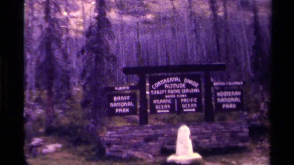 1979 8mm frame of the Continental Divide marker between Banff and Kootenay National Parks, seen through a purple color cast.