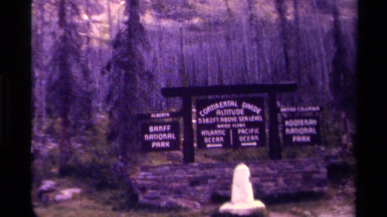 Wooden Continental Divide sign with forest, stone base, and white marker in front.