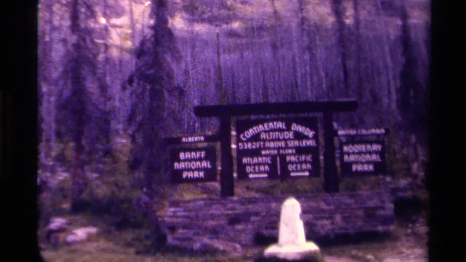 Canadian park boundary sign for the Continental Divide, with Banff and Kootenay panels visible on soft 8mm footage.