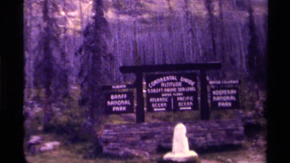 8mm home-movie view of the Continental Divide sign, including readable Banff and Kootenay National Park panels.