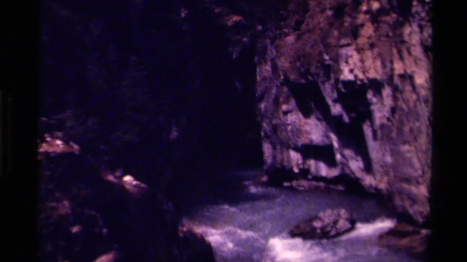 1979 Canada 8mm view of pale rapids passing between dark canyon walls and a rough rock face.