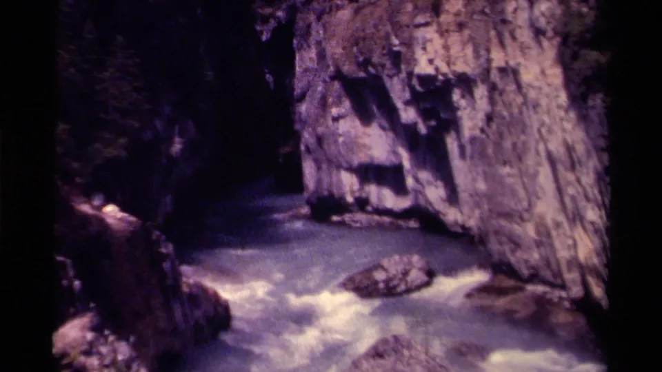 1979 Canadian 8mm frame showing fast blue-green water moving through a shadowed rocky gorge with cliff faces on both sides.