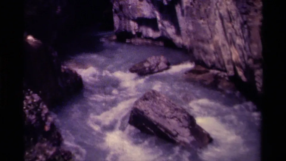 1979 Canadian 8mm frame showing foaming river water passing a large foreground boulder in a narrow mountain gorge.