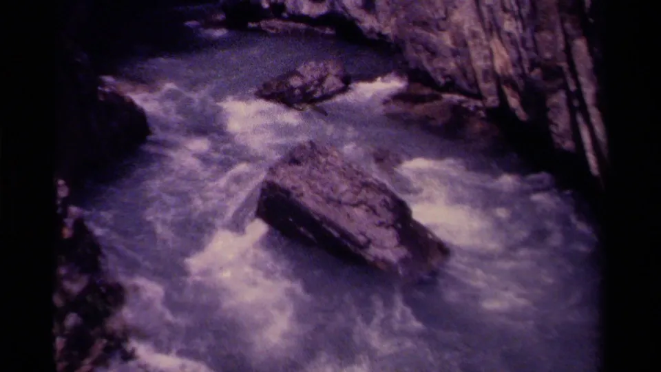 1979 Canadian 8mm frame of swift water breaking around large rocks within a steep, shadowed gorge.