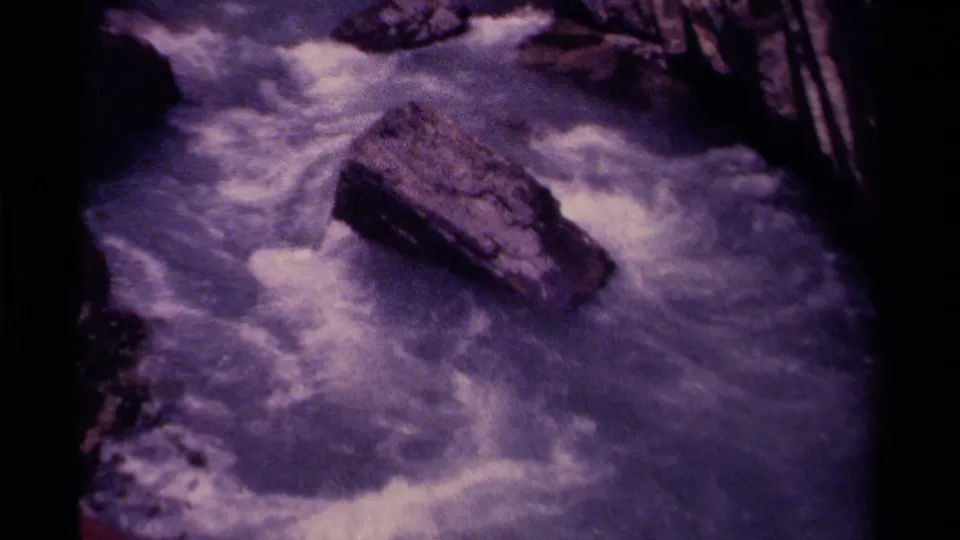 1979 8mm home-movie view in Canada of rushing stream water churning around a large rock in a rugged canyon.