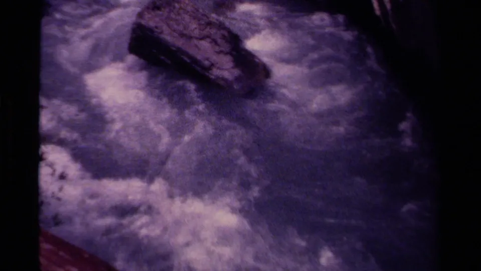 Purple-tinted 8mm footage shows a rocky Canadian stream with whitewater moving through a narrow natural channel.
