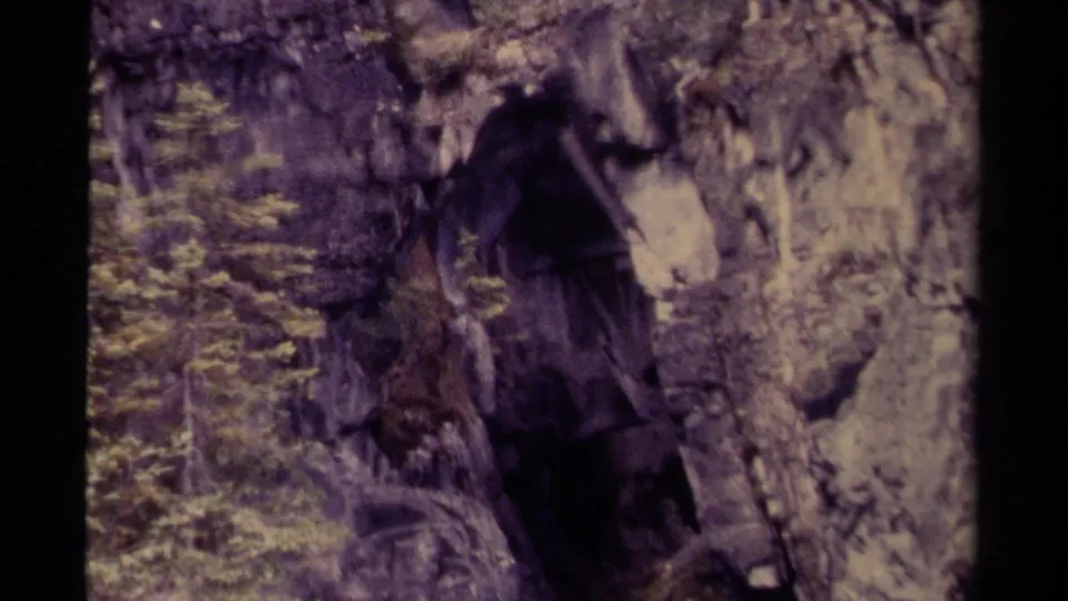 1979 Canadian 8mm view of a rugged stone passage with a dark cavern entrance and vegetation at the edge.