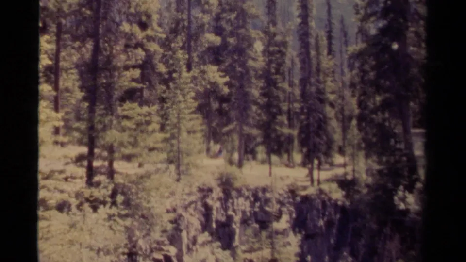1979 Canadian 8mm frame showing a rocky cliff edge, conifer forest, and distant mountain landscape.