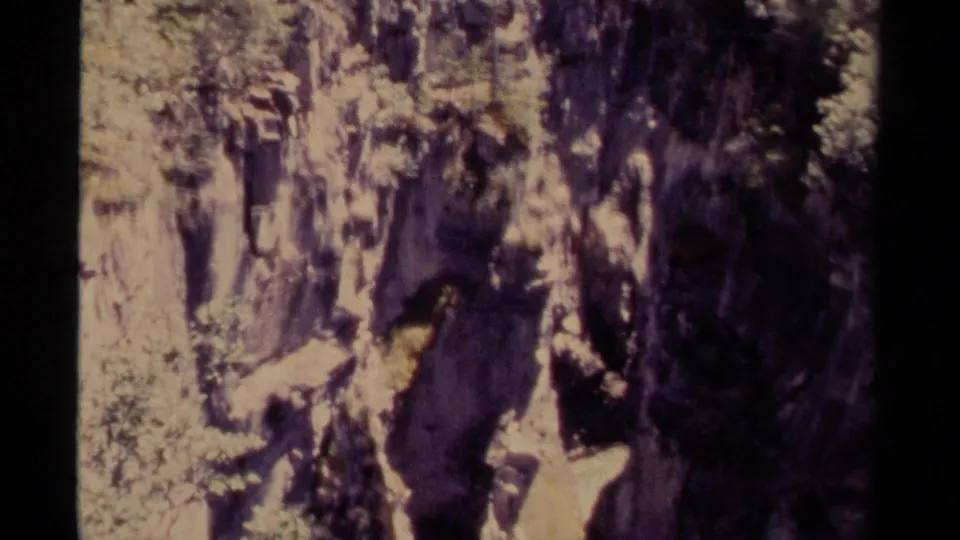 1979 Canada 8mm frame showing a rugged gorge with pale stone, deep shadow, scattered brush, and trees near the rim.