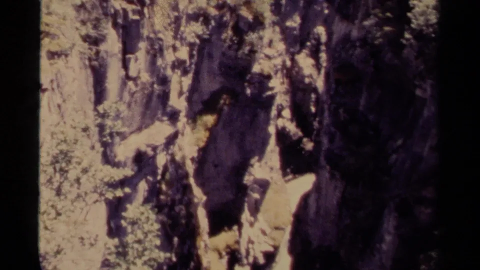 1979 Canada 8mm frame capturing a shadowed canyon section, steep rock walls, shrubs, and pine trees in bright daylight.