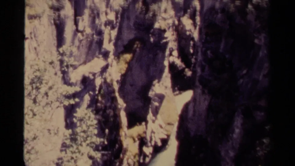 1979 Canadian 8mm frame showing pale flowing water beside dark rock walls, sunlit stone, and patches of green foliage.
