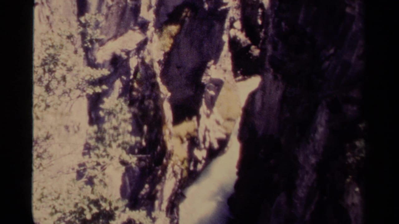 Rocky canyon view with bright water channel, dark cliff face, and foliage at the edge.