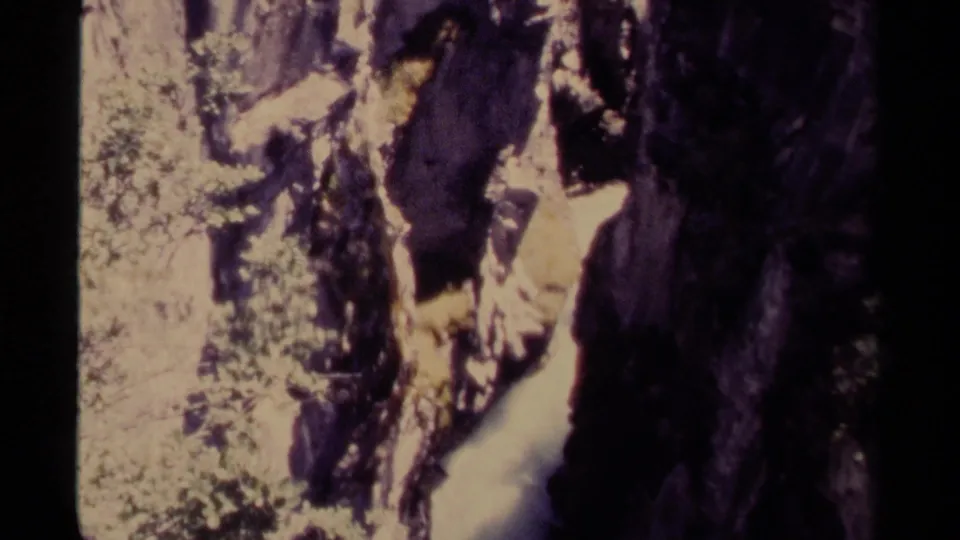 1979 Canadian 8mm view of a narrow canyon where bright water passes below steep, shadowed rock and scattered foliage.