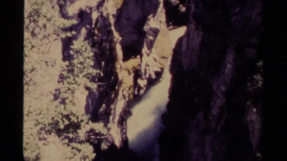1979 Canadian 8mm frame of white water moving through a rocky gorge, bordered by dark cliff surfaces and leafy growth.