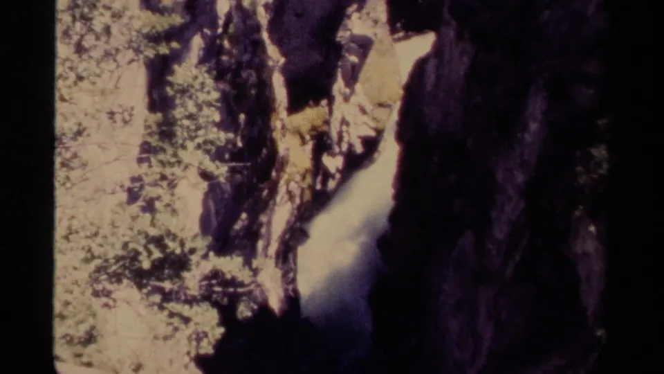 1979 Canadian 8mm frame showing pale rushing water in a narrow rocky canyon with deep shadow and small areas of foliage.