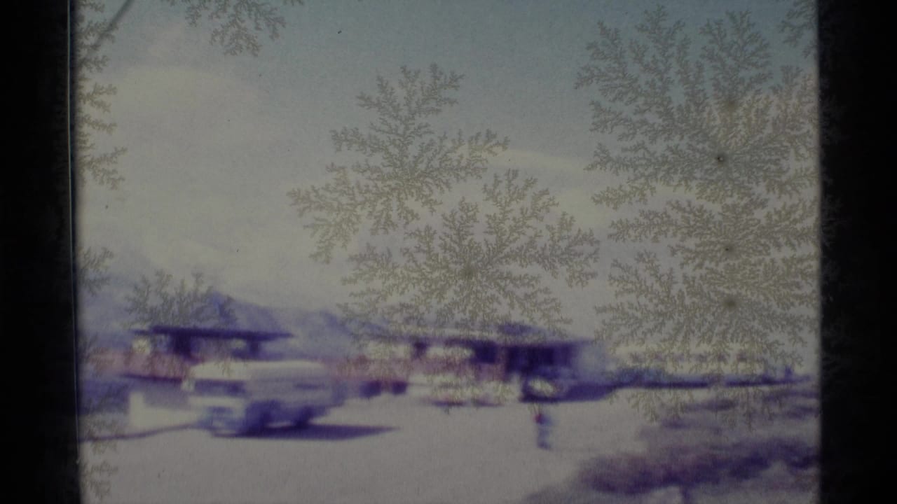 Frost-covered window view of cars and small buildings near mountains.