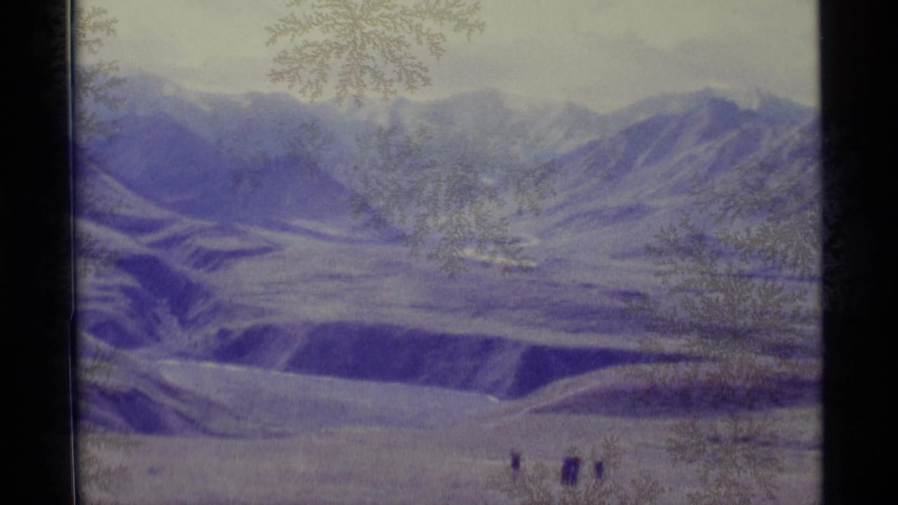 Snowy mountain range and valley with tiny figures near the bottom of the frame.