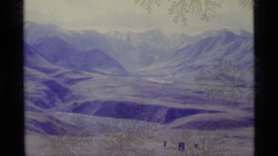 1977 Alaska 8mm view of mountain slopes and a snowy valley, with distant hikers visible near the bottom edge.
