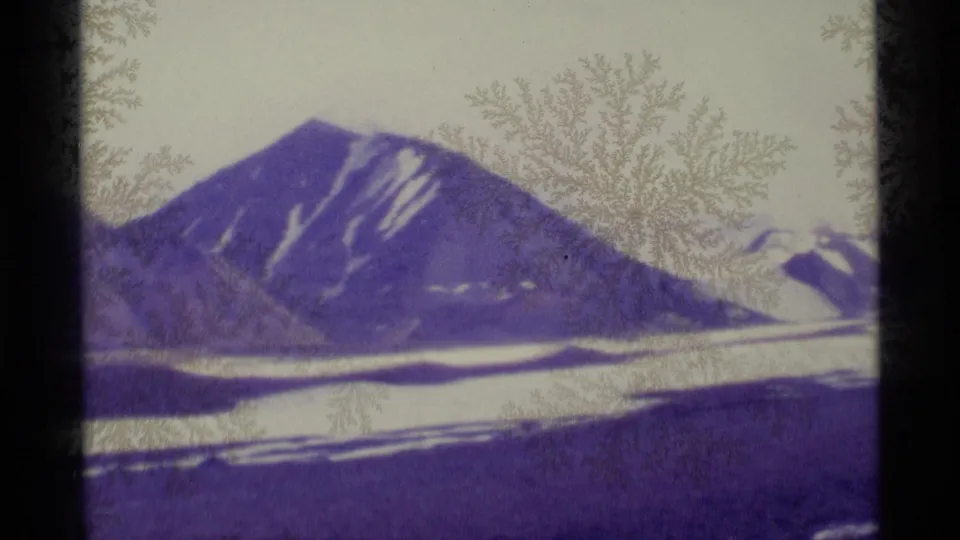 1977 Alaska 8mm frame shows a snow-streaked mountain above a bright snowfield, with crystalline marks visible on the lens.