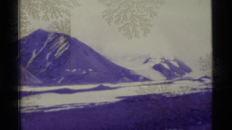 1977 Alaska 8mm frame showing snow-capped mountains under a pale sky with visible film-surface frost patterns.