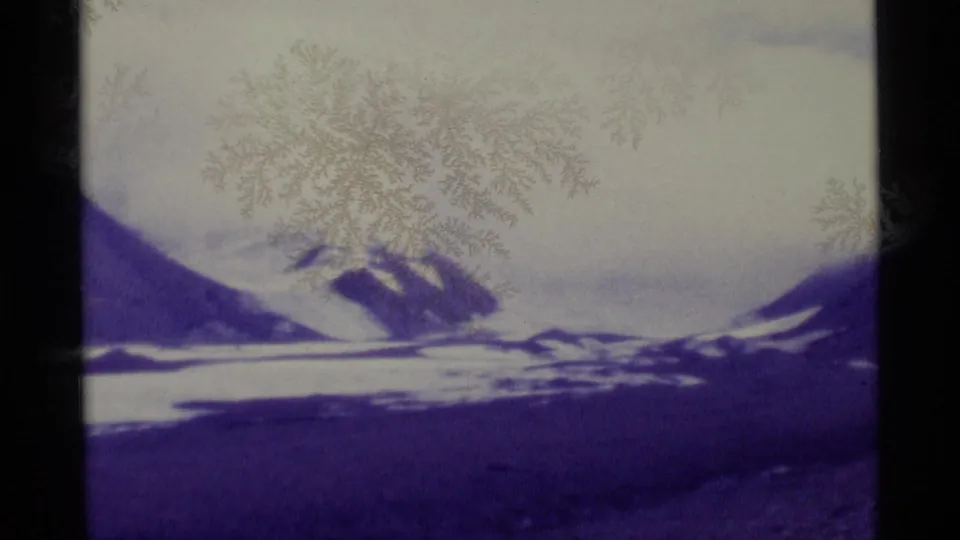 1977 Alaska home-movie frame with distant snow-covered peaks, purple terrain, pale sky, and visible film borders.