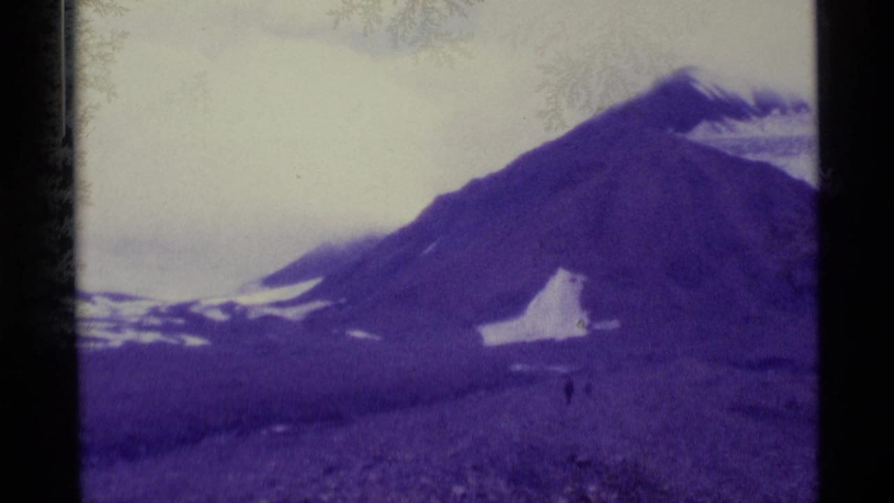 1977 Alaska 8mm frame showing a rocky mountain slope, scattered snow, soft focus, and visible film gate borders.