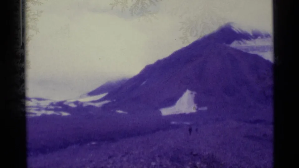 1977 Alaska 8mm frame showing a rocky mountain slope, scattered snow, soft focus, and visible film gate borders.
