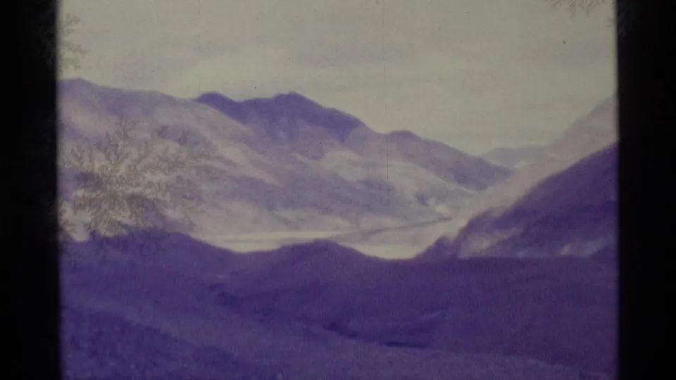 1977 Alaska 8mm frame of a wide mountain valley with ridgelines, snow patches, and visible frost-like desiccant marks.