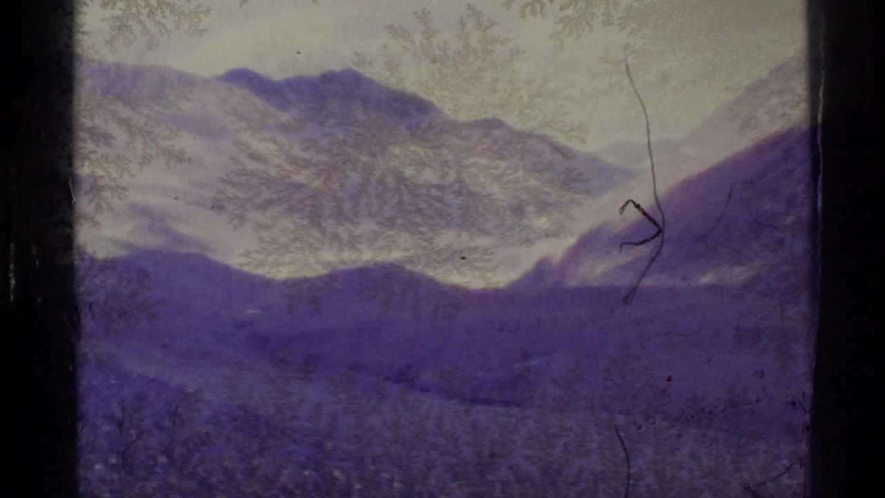1977 Alaska 8mm frame showing a purple-shifted mountain valley with snow patches, gate edges, and frost-like film texture.