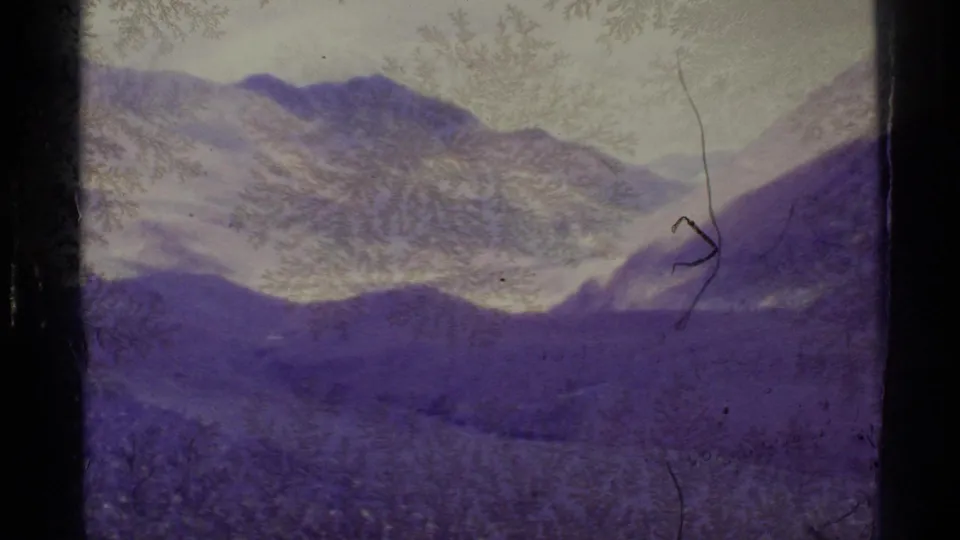 1977 Alaska 8mm frame showing a purple-shifted mountain valley with snow patches, gate edges, and frost-like film texture.
