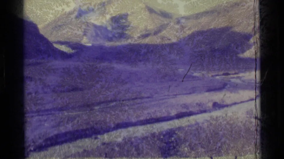 1977 Alaska 8mm frame showing a color-shifted mountain valley with possible water or track line and visible scratches.