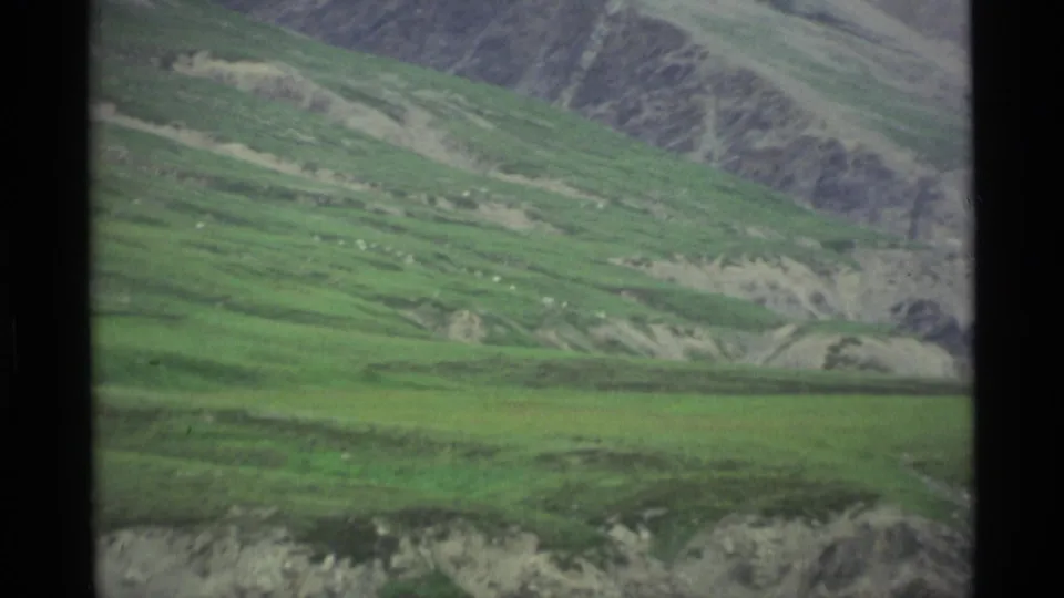 1977 Alaska 8mm landscape frame with green mountain slopes, exposed rocky ground, and muted home-movie color.