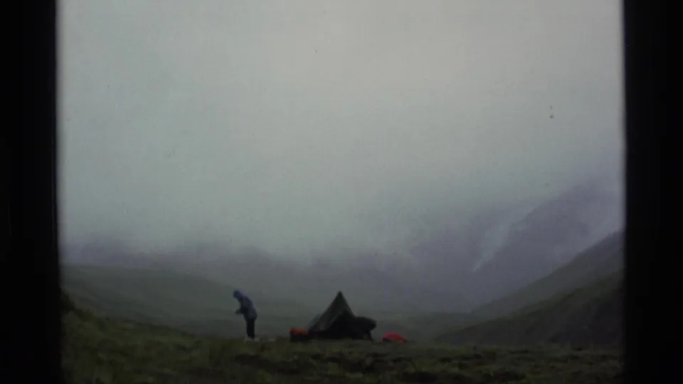 1977 Alaska 8mm frame showing a lone distant camper near a tent, with low cloud obscuring the surrounding mountain slopes.