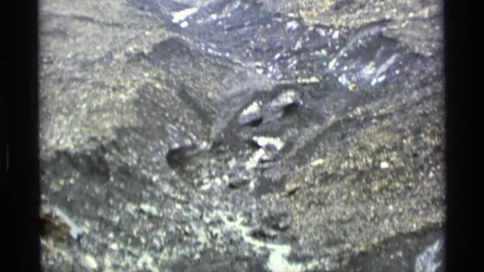 1977 Alaska 8mm frame of rough mountain terrain with exposed rock, scree, and lingering snow patches.